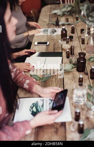 Die weibliche Kollegen sitzen aus der hohen Perspektive am Tisch Mit verschiedenen Parfümflaschen und Broschüren in der Werkstatt Stockfoto