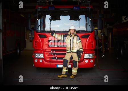 In voller Länge Porträt von lächelnden weiblichen Feuerwehrmann vor stehen Des Feuerwehrmotors in der Feuerwache Stockfoto