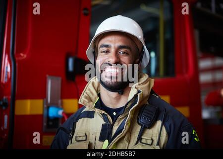 Portrait eines lächelnden Feuerwehrmichters mit Helm, der an der Feuerwehr steht Stockfoto