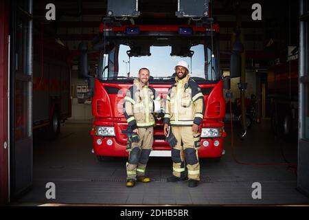 Portrait der Feuerwehrleute, die vor dem Feuerwehrmotor stehen Feuerwehrhaus Stockfoto