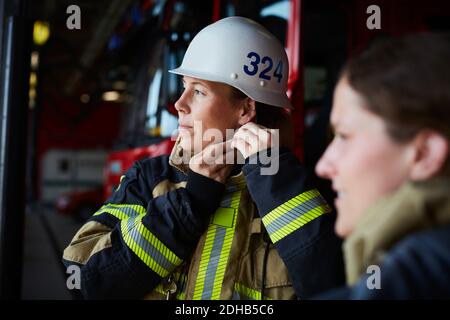 Feuerwehrfrau mit Helm im Stehen mit Mitarbeiterin in Brand Station Stockfoto