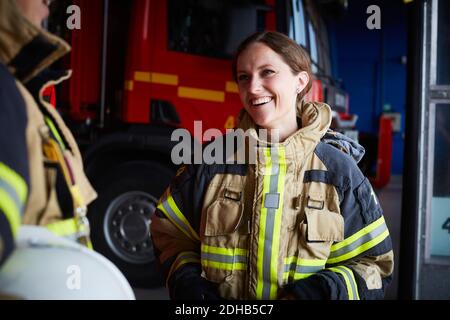 Lächelnde Feuerwehrfrau, die beim Kommunizieren im Feuer auf die Mitarbeiterin schaut Station Stockfoto