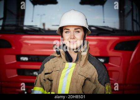 Portrait der Feuerwehrfrau trägt Helm gegen Feuerwehrmann bei Feuerwehrhaus Stockfoto