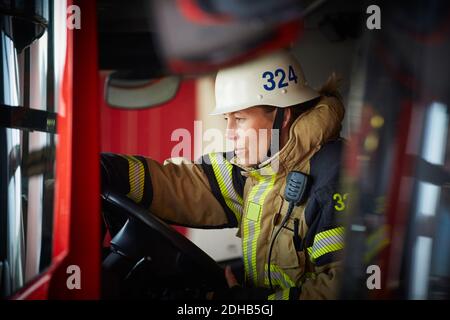 Feuerwehrfrau trägt Helm im Feuerwehrauto bei Feuer sitzen Station Stockfoto