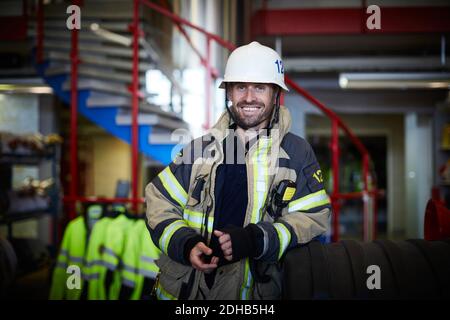 Porträt eines lächelnden Feuerwehrmichters in Schutzanzug an der Feuerwehr Stockfoto