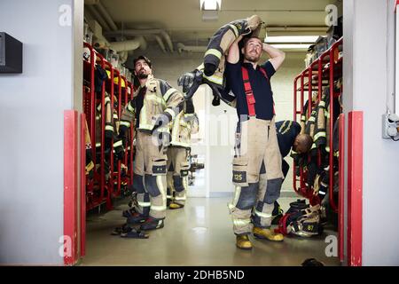 Feuerwehrleute tragen Arbeitsschutzkleidung im Umkleideraum, während sie nach oben schauen An der Feuerwehr Stockfoto