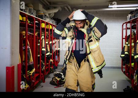 Mittlerer Erwachsener Feuerwehrmann trägt Arbeitshelm im Umkleideraum bei Feuerwehrhaus Stockfoto