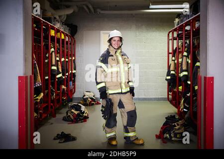 In voller Länge Porträt von lächelnden weiblichen Feuerwehrmann im Schrank stehen Raum an der Feuerwache Stockfoto