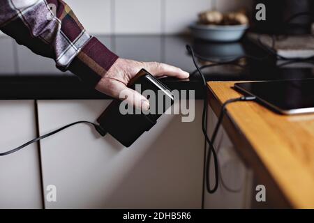 Kurze Hände eines älteren Mannes, der in der Küche ein Smartphone hält Zähler Stockfoto