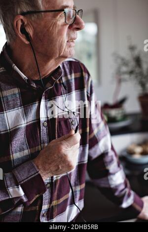 Ein älterer Mann schaut weg, während er mit dem Smartphone spricht In-Ear-Kopfhörer in der Küche zu Hause Stockfoto