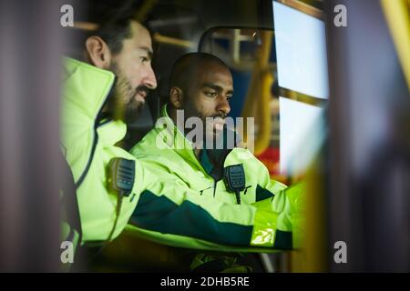 Männliche Sanitäter diskutieren, während sie im Krankenwagen auf dem Parkplatz sitzen Stockfoto