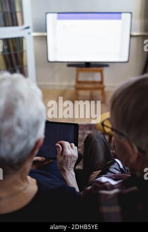Rückansicht eines älteren Ehepaares mit digitaler Tablet-Beobachtung Fernseher zu Hause Stockfoto