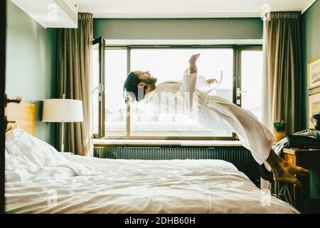 Verspielter Mann in Robe, der im Hotel auf dem Bett springt Stockfoto