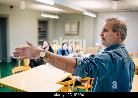 Älterer männlicher Lehrer, der während des Unterrichts im Klassenzimmer gestikiert Stockfoto