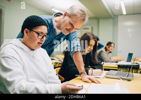 Männlicher Lehrer, der Schüler am Schreibtisch im Klassenzimmer unterstützt Stockfoto