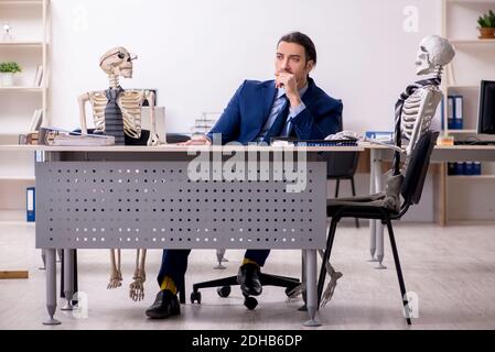 Junger männlicher Angestellter mit Skeletten im Büro Stockfoto