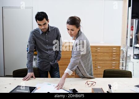 Selbstbewusste männliche und weibliche Geschäftskollegen diskutieren über Dokumente bei Tisch im Büro Stockfoto