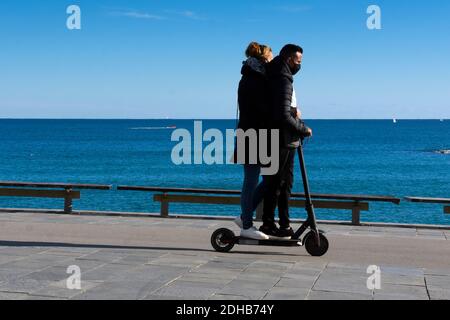 Ein junges Paar reitet auf dem gleichen Elektroroller zusammen entlang der Promenade. Stockfoto