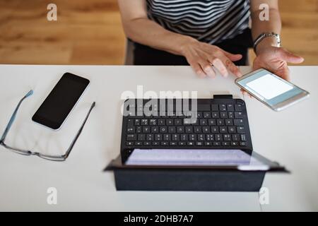 Mittelteil der mittleren erwachsenen Frau mit Laptop und Smartphone Am Tisch Stockfoto