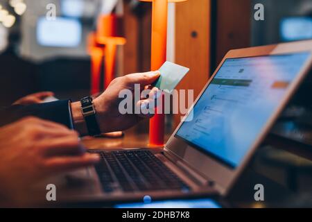 Zugeschnittenes Bild des Geschäftsmannes, der während der Verwendung eines Laptops eine Kreditkarte hält Am Flughafen Stockfoto
