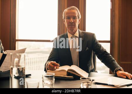 Portrait eines selbstbewussten, reifen Rechtsanwalts mit Buch am Konferenztisch Im Büro Stockfoto