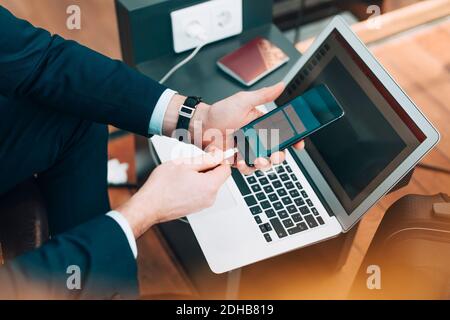 Zugeschnittenes Bild von Geschäftsmann stecken USB-Kabel in Handy Am Flughafen Stockfoto