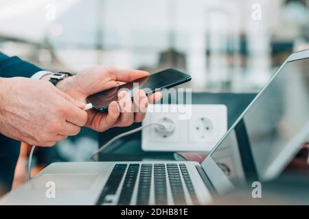 Zugeschnittenes Bild von Geschäftsmann stecken USB-Kabel in Smartphone Am Flughafen Stockfoto