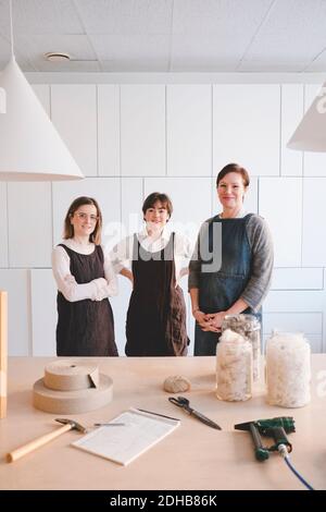 Portrait von selbstbewussten Design-Profis tragen Schürzen mit verschiedenen Geräten Auf dem Schreibtisch in der Werkstatt Stockfoto