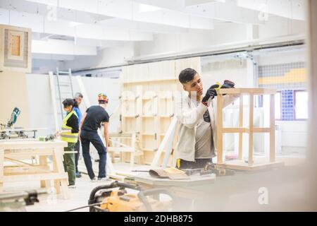 Selbstbewusster männlicher Teenager-Auszubildender, der Sandpapier auf Holztisch reibt An der Werkbank Stockfoto