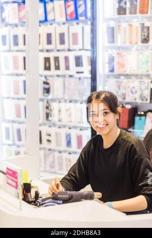 Porträt einer selbstbewussten jungen Mitarbeiterin, die lächelt, während sie ansitzt Beleuchteter Schreibtisch im Geschäft Stockfoto