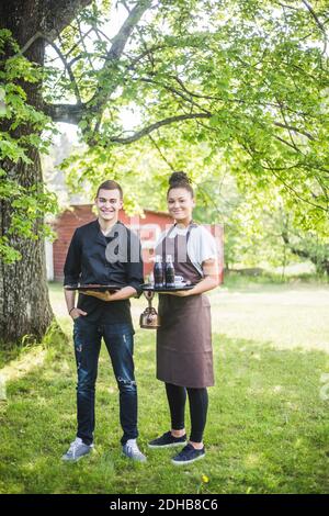 Full Länge Porträt von lächelnd zuversichtlich jungen Mann und Frau Kellner stehen auf Gras im Cafe im Freien Stockfoto