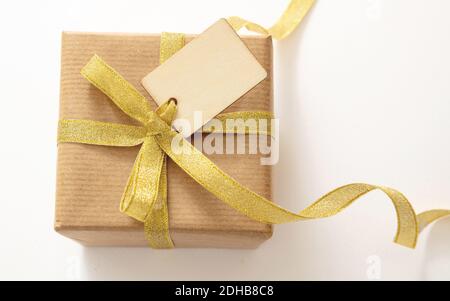 Geschenkbox mit einem leeren Tag isoliert auf weißem Hintergrund, Draufsicht. Kraftpapier Recycling braun Papierverpackung mit Gold glänzend Band, Weihnachtsgeschenk Vorlage, Stockfoto