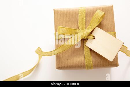 Geschenkbox mit einem leeren Tag isoliert auf weißem Hintergrund, Draufsicht. Kraftpapier Recycling braun Papierverpackung mit Gold glänzend Band, Weihnachtsgeschenk Vorlage, Stockfoto