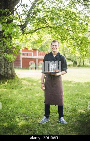 In voller Länge Porträt von lächelnden selbstbewussten jungen Kellner stehen auf Gras im Cafe im Freien Stockfoto
