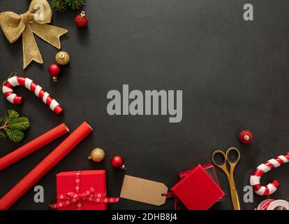 Weihnachtsgeschenke Vorbereitung. Geschenkschachteln Verpackung flach lag auf schwarzem Hintergrund, Draufsicht. Rote Farbverzierungen und Zubehör, Kartenschablone, Kopie Stockfoto