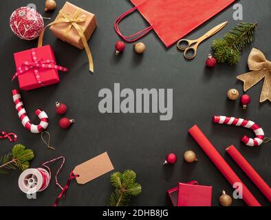 Weihnachtsgeschenke Vorbereitung. Geschenkschachteln Verpackung flach lag auf schwarzem Hintergrund, Draufsicht. Rote Farbverzierungen und Zubehör, Kartenschablone, Kopie Stockfoto