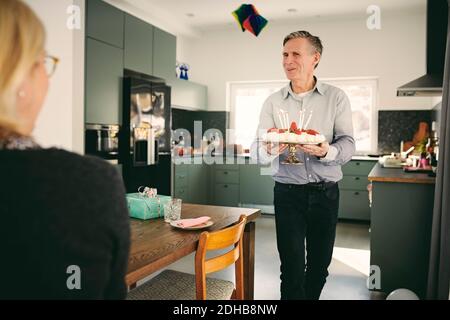 Frau, die beim Gehen auf einen älteren Mann schaut, der Geburtstagskuchen hält Nach Tabelle Stockfoto