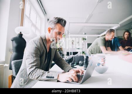 Selbstbewusster Geschäftsmann mit Laptop am Schreibtisch im kreativen Büro Stockfoto