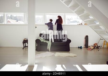 Ganze Länge von Geschwistern, die auf dem Sofa stehen, während sie durchschauen Fenster zu Hause Stockfoto