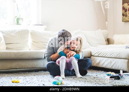 Mid adult Mann küssen Tochter während sitzen auf Teppich an Zu Hause Stockfoto