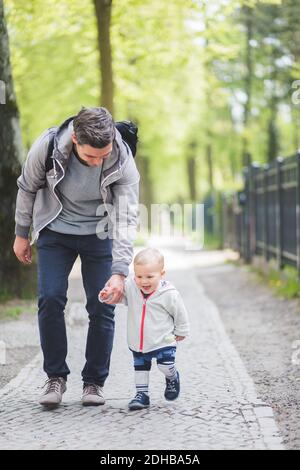 Die ganze Länge von Vater und Sohn halten Hände beim Gehen Auf Fußweg Stockfoto