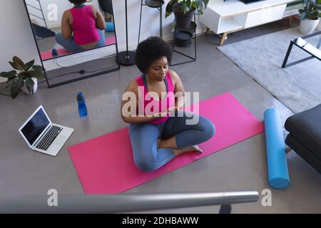 afroamerikanische Frau tun Yoga-Meditation sitzen auf Matte tragen Sportkleidung. Laptop im Hintergrund. Selbstisolation Fitness Wohlbefinden technol Stockfoto