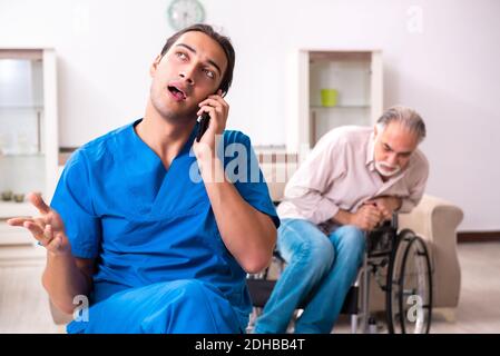 Alter Mann im Rollstuhl und junge schlechte Betreuer drinnen Stockfoto