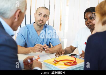 Ärzte hören dem Paar zu, während sie während des Besuchs am Tisch sitzen Im Krankenhaus Stockfoto
