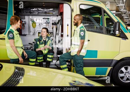 Männliche und weibliche Sanitäter sprechen, während sie im Krankenwagen sitzen Parkplatz Stockfoto