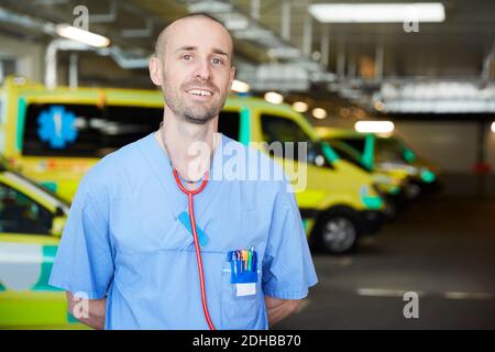 Porträt eines lächelnden männlichen Arztes mit Stethoskop gegen Krankenwagen in Parkplatz Stockfoto