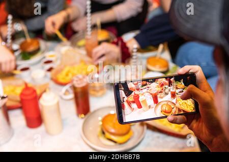 Zugeschnittenes Bild eines Teenagers, der Essen und Getränke fotografiert Auf dem Tisch im Restaurant Stockfoto