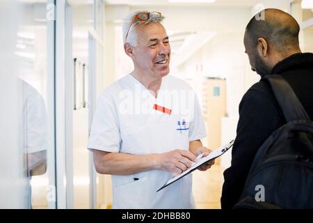 Lächelnder männlicher Arzt erklärt medizinischen Bericht zu männlichen Patienten während Routinebesuch in der Klinik Stockfoto