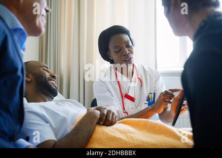 Ärztin erklärt Patientenakte über digitale Tablette Und Familie in der Krankenstation Stockfoto