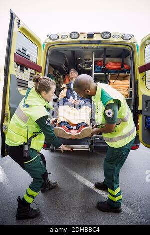 Die gesamte Länge der männlichen und weiblichen Sanitäter, die den Patienten aus der Entladung entlassen Krankenwagen Stockfoto